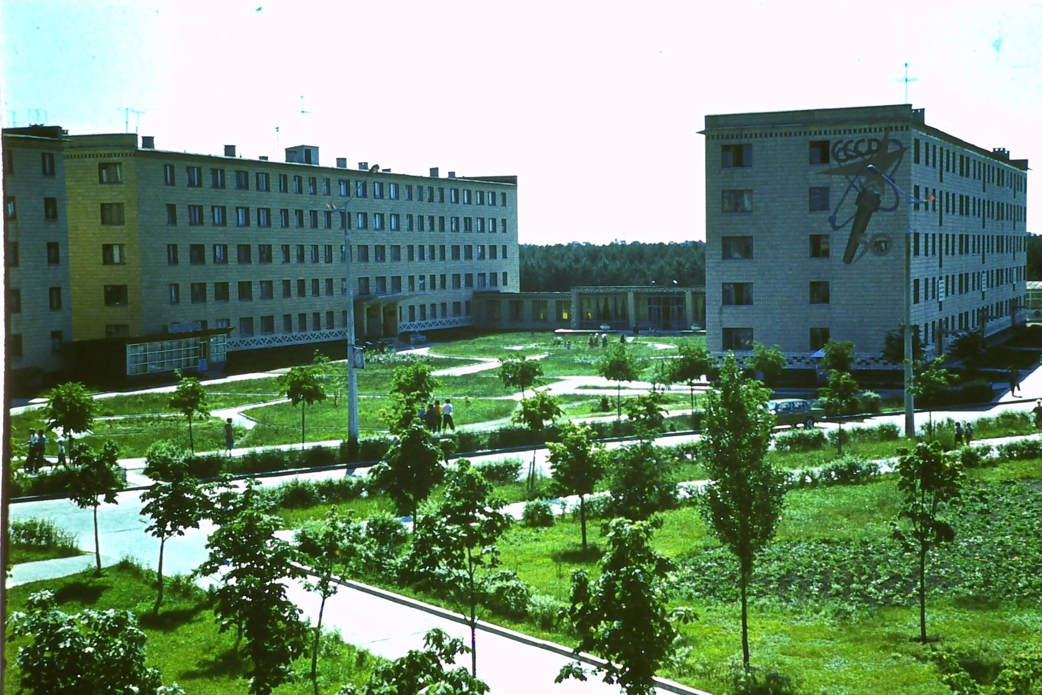 Prypeć, ul. Przyjaźni Narodów. Budynki hoteli pracowniczych: nr 3 (po lewej) oraz nr 4 (po prawej z namalowana na fasadzie pochodnią z napisem 50 лет symbolizującym 50 lat ZSRR (1922 - 1972). Widoczny pomiędzy budynkami parterowy pawilon to biblioteka pracownicza, w głębi stołówka nr 5 „Drużba” („Przyjaźń”).  